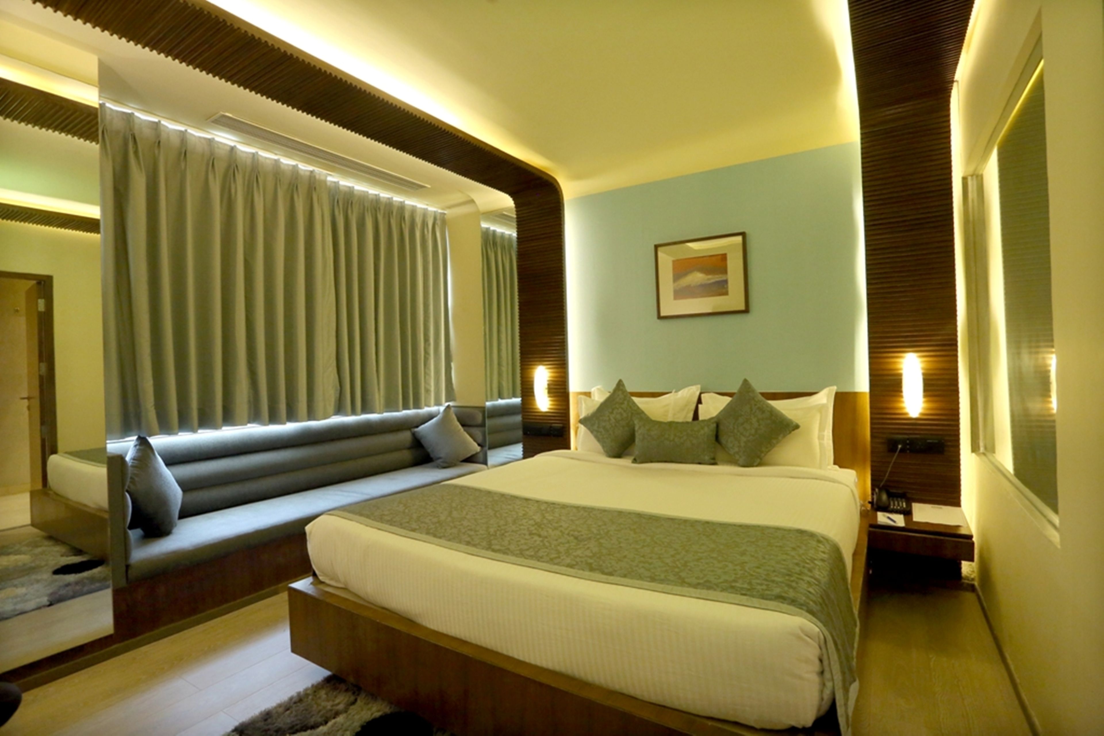 Una habitación de hotel moderna con una cama grande, un sofá cama, una mesita de noche y una ventana con cortinas.
