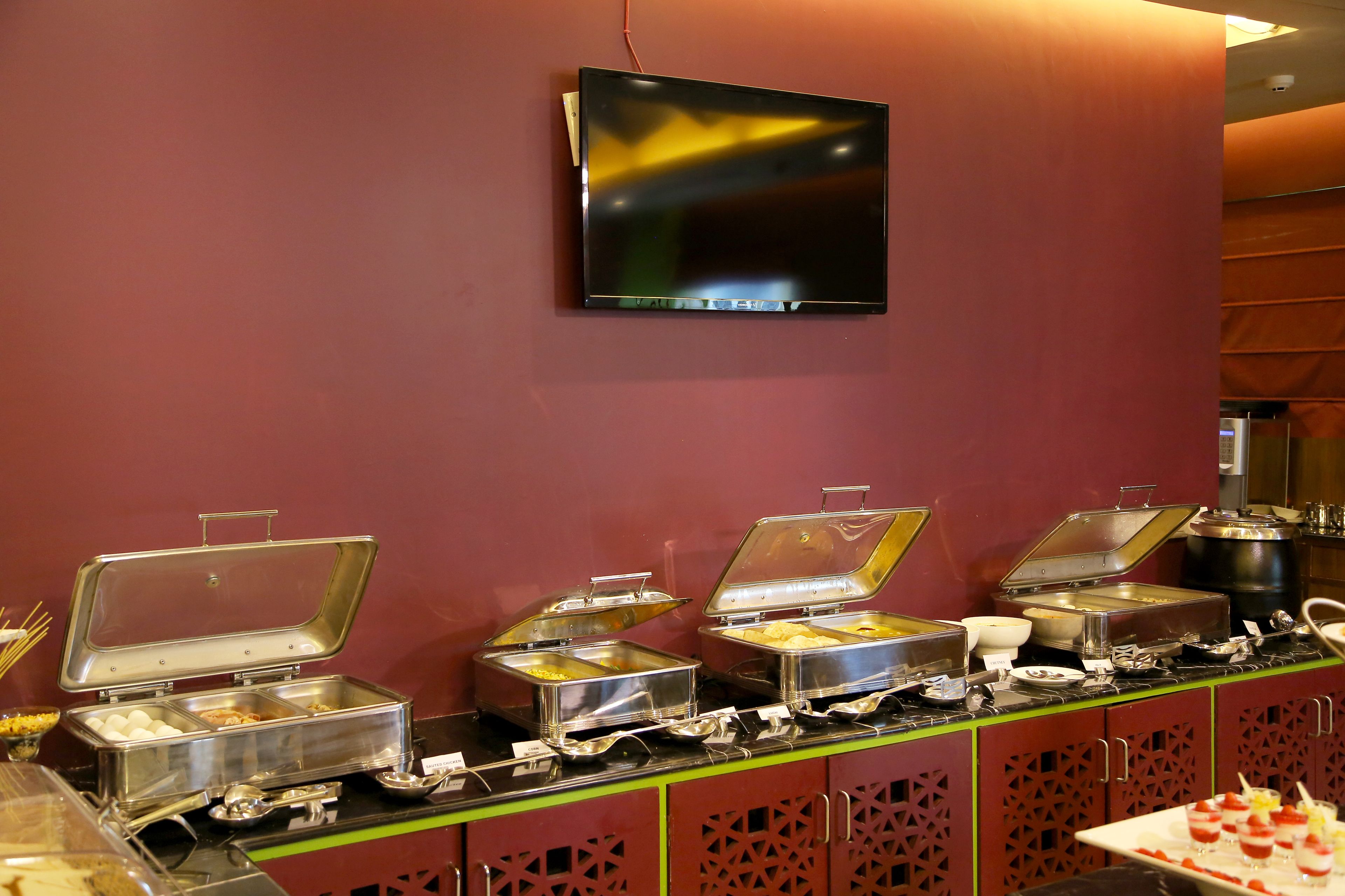 A buffet setup with multiple food containers and a television mounted on the wall.