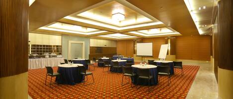 A conference room with a patterned carpet, round tables, and chairs, equipped with a projector screen and a whiteboard.