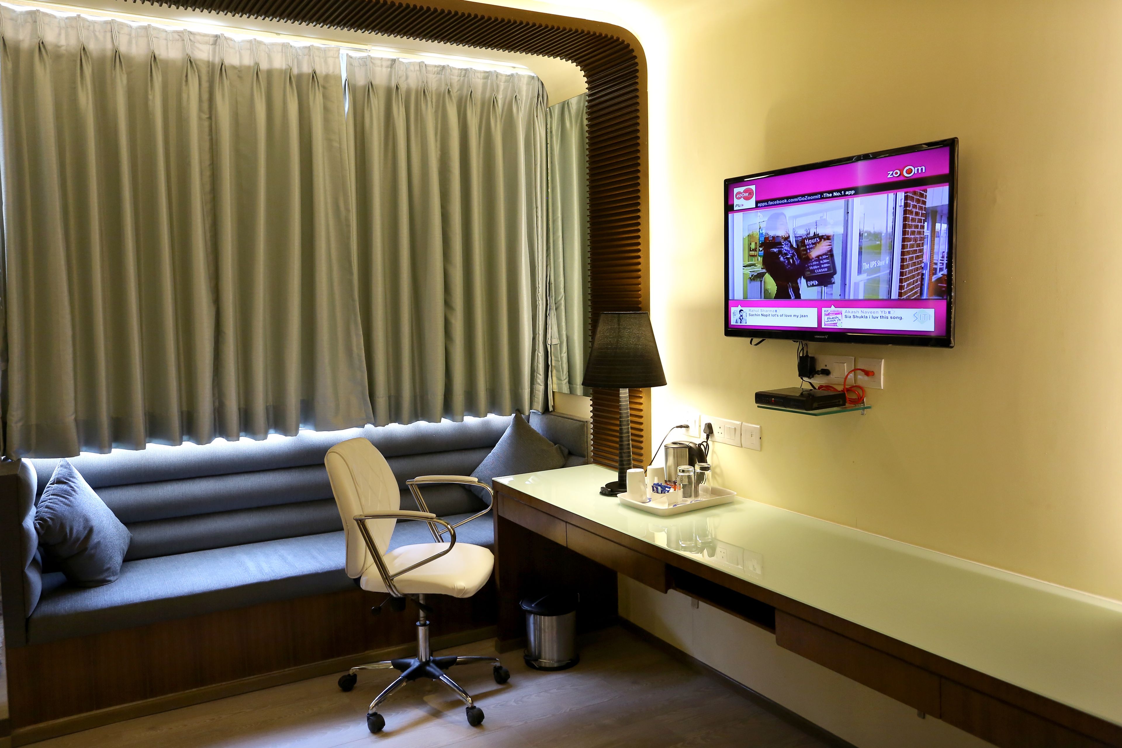 A modern hotel room with a sofa, desk, and TV.
