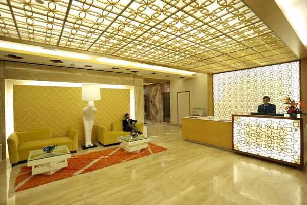 Un hall de hotel con una recepción, un sofá amarillo, una estatua blanca y un papel tapiz estampado.