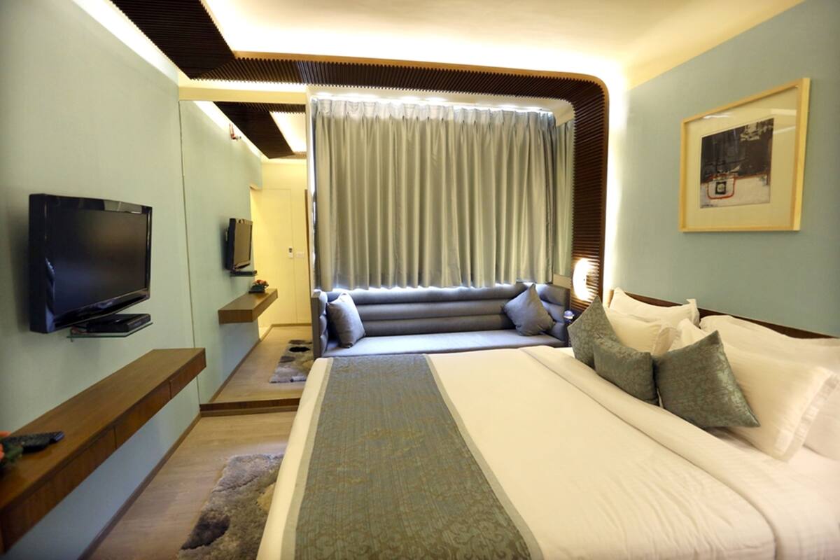 A hotel room with a large bed, a flat-screen TV mounted on the wall, a sofa, and a framed picture on the wall.