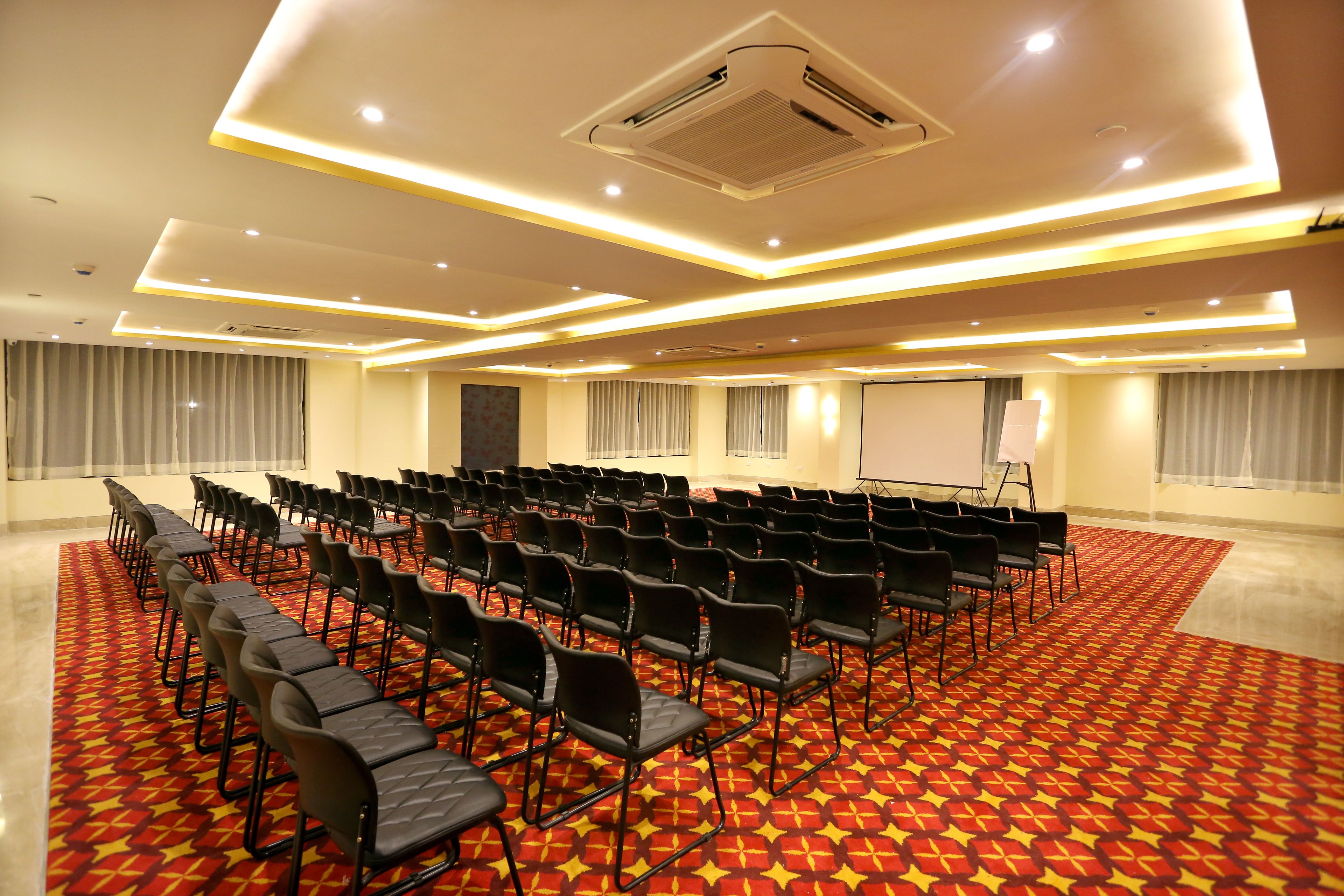 A conference room with rows of chairs, a projector screen, and a carpeted floor.