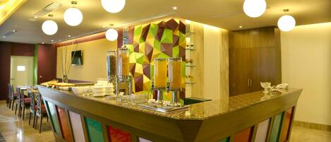 A hotel reception area with a colorful counter, multiple juice dispensers, and a phone.