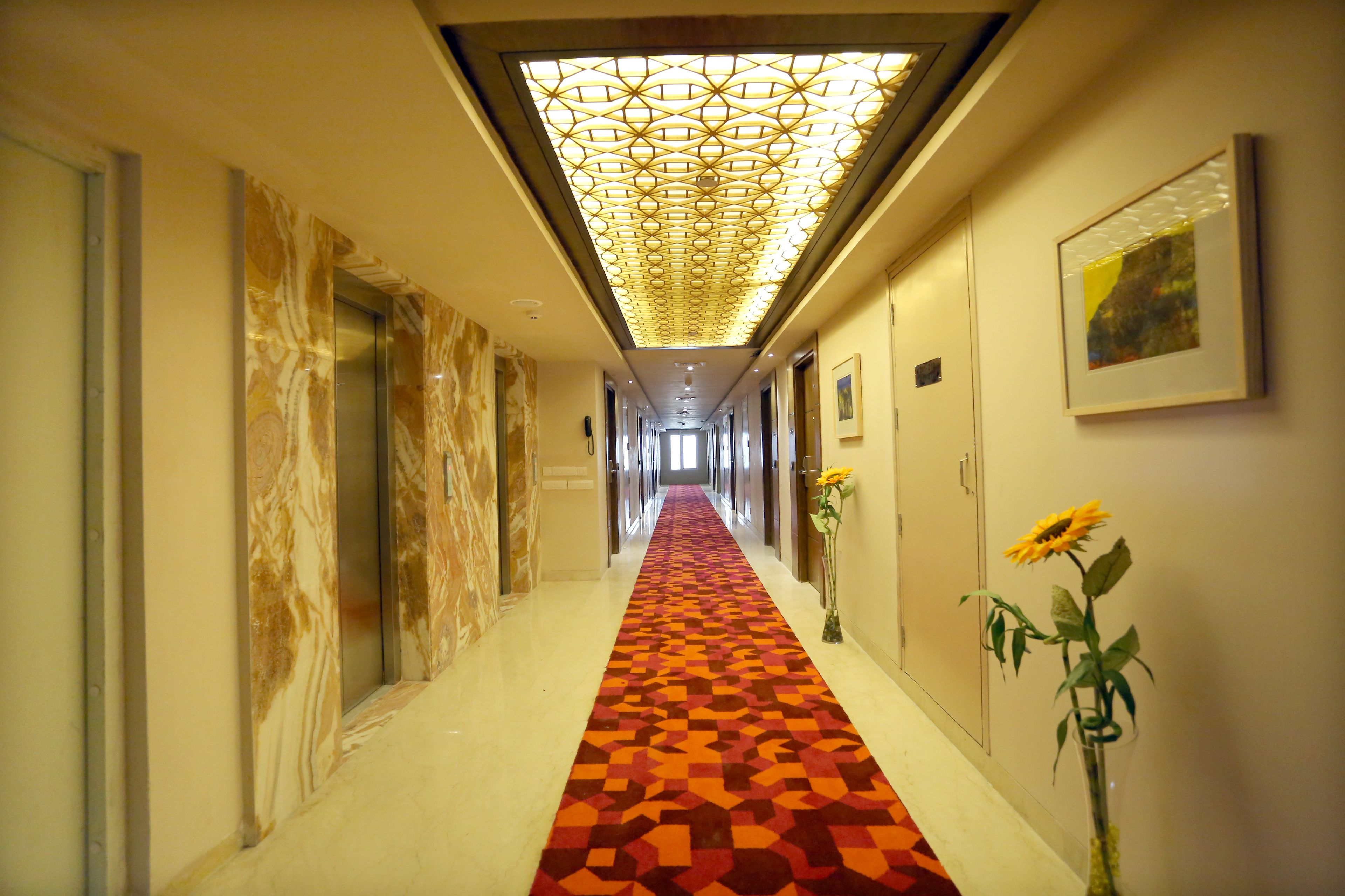 A hotel hallway with a patterned carpet, marble walls, and a ceiling light fixture.