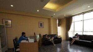A hotel lobby with a reception desk, a black leather sofa, and a large window with curtains.
