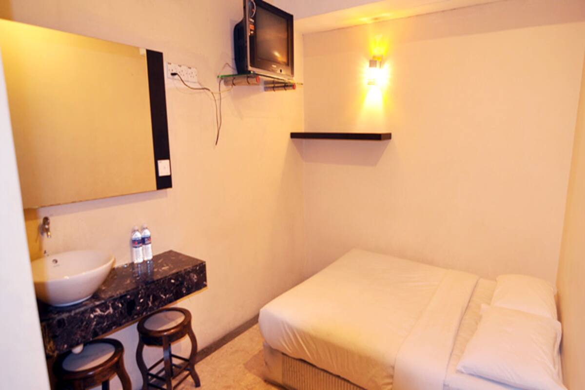 Una habitación pequeña con cama individual y baño que incluye un lavamanos y un espejo.
