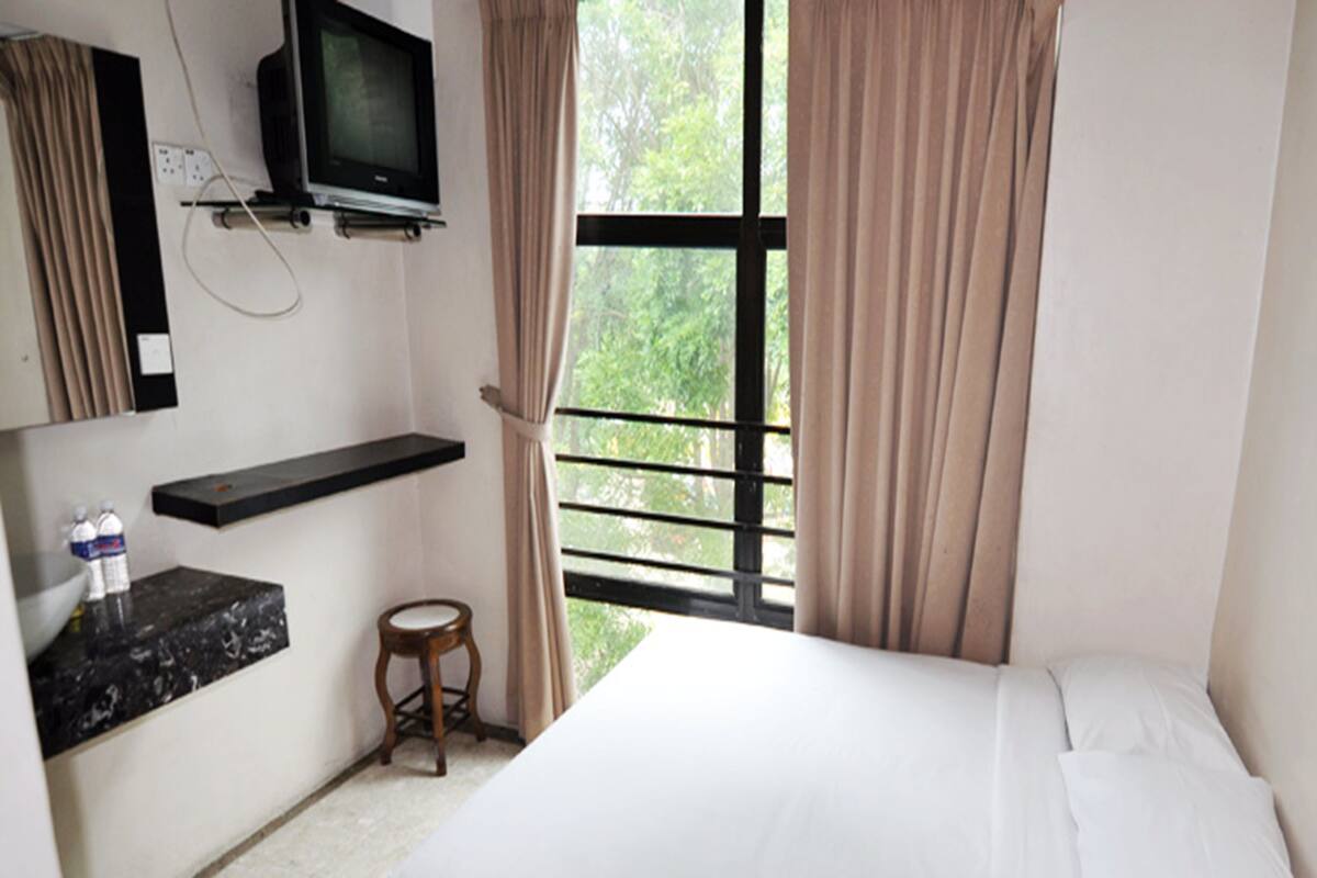 Habitación de hotel con cama, televisor montado en la pared, un taburete pequeño y una ventana con cortinas.