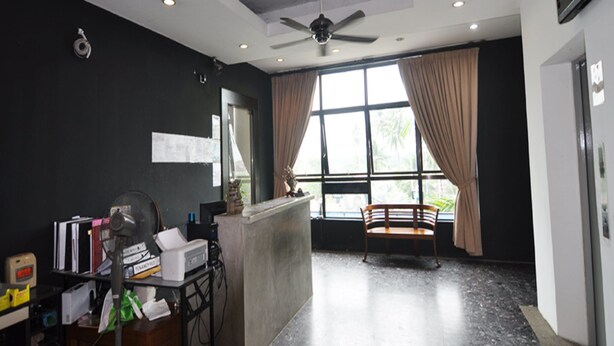 A reception area with a desk, computer, and chair. There is a window with curtains and a view of greenery outside.