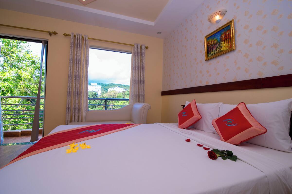 A hotel room with a large bed, a balcony with a view, and a painting on the wall.