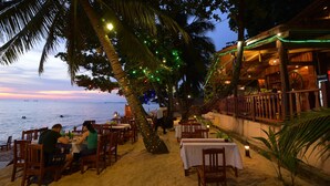 An outdoor dining area with tables and chairs, palm trees, and a view of the sea. - Kim Hoa Resort (Phu Quoc)