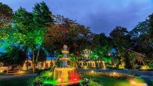 A well-lit garden with a fountain, surrounded by trees and a building in the background. - Kim Hoa Resort (Phu Quoc)