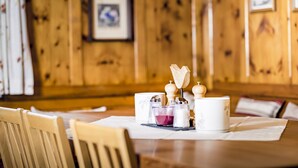 Una habitación con paneles de madera, con una mesa de comedor dispuesta para dos personas, incluyendo saleros y pimenteros, una vela y un recipiente blanco.