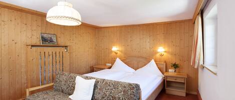 A wooden-paneled room with a bed, a sofa, and a nightstand with a lamp.