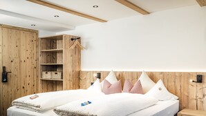 Una habitación de hotel moderna con cabecera de madera, una cama grande con ropa blanca, un armario de madera y una mesita de noche de madera.