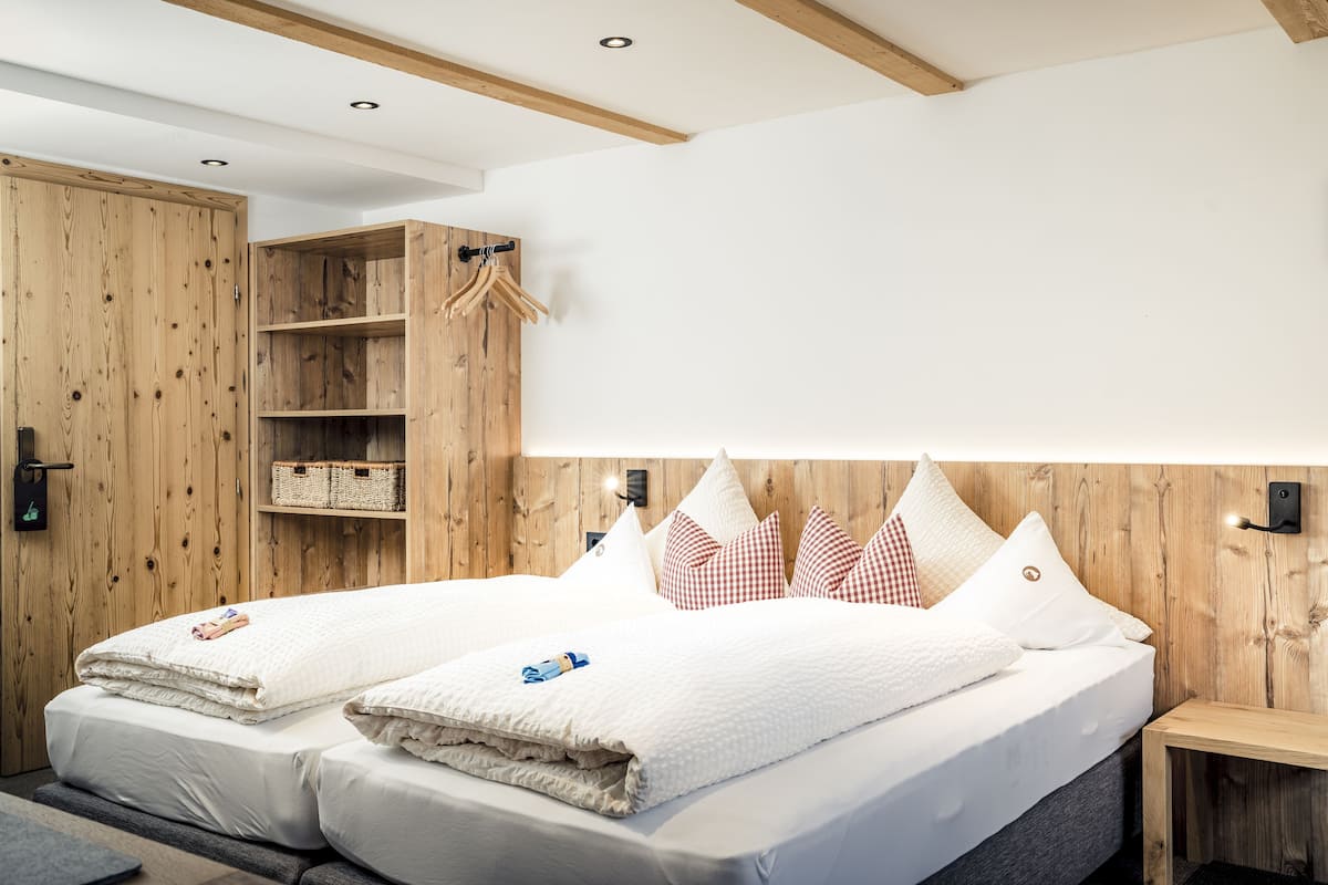 Una habitación de hotel moderna con cabecera de madera, una cama grande con ropa blanca, un armario de madera y una mesita de noche de madera.