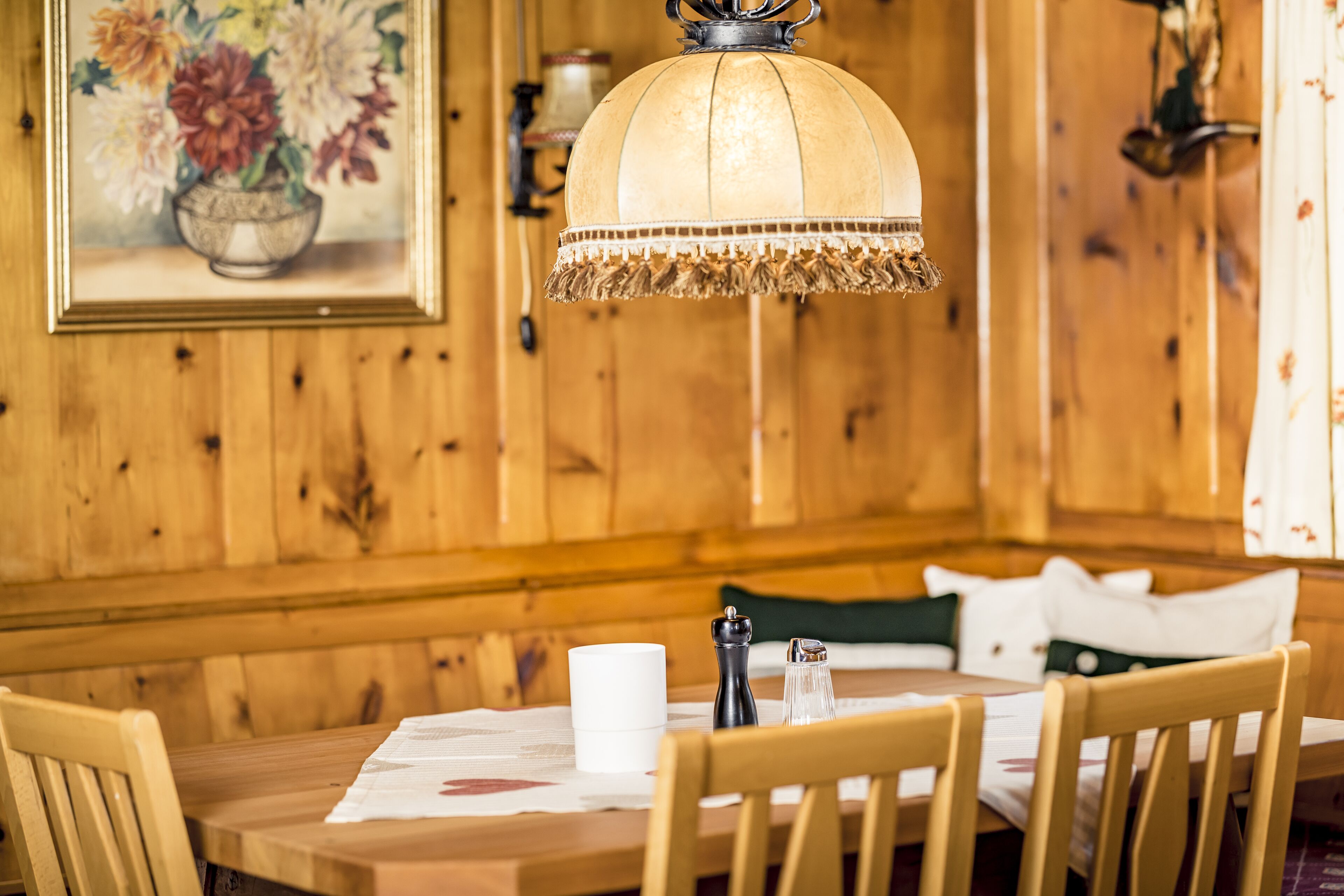 A wooden dining table with chairs, a white cup, a salt and pepper shaker, and a hanging lamp.