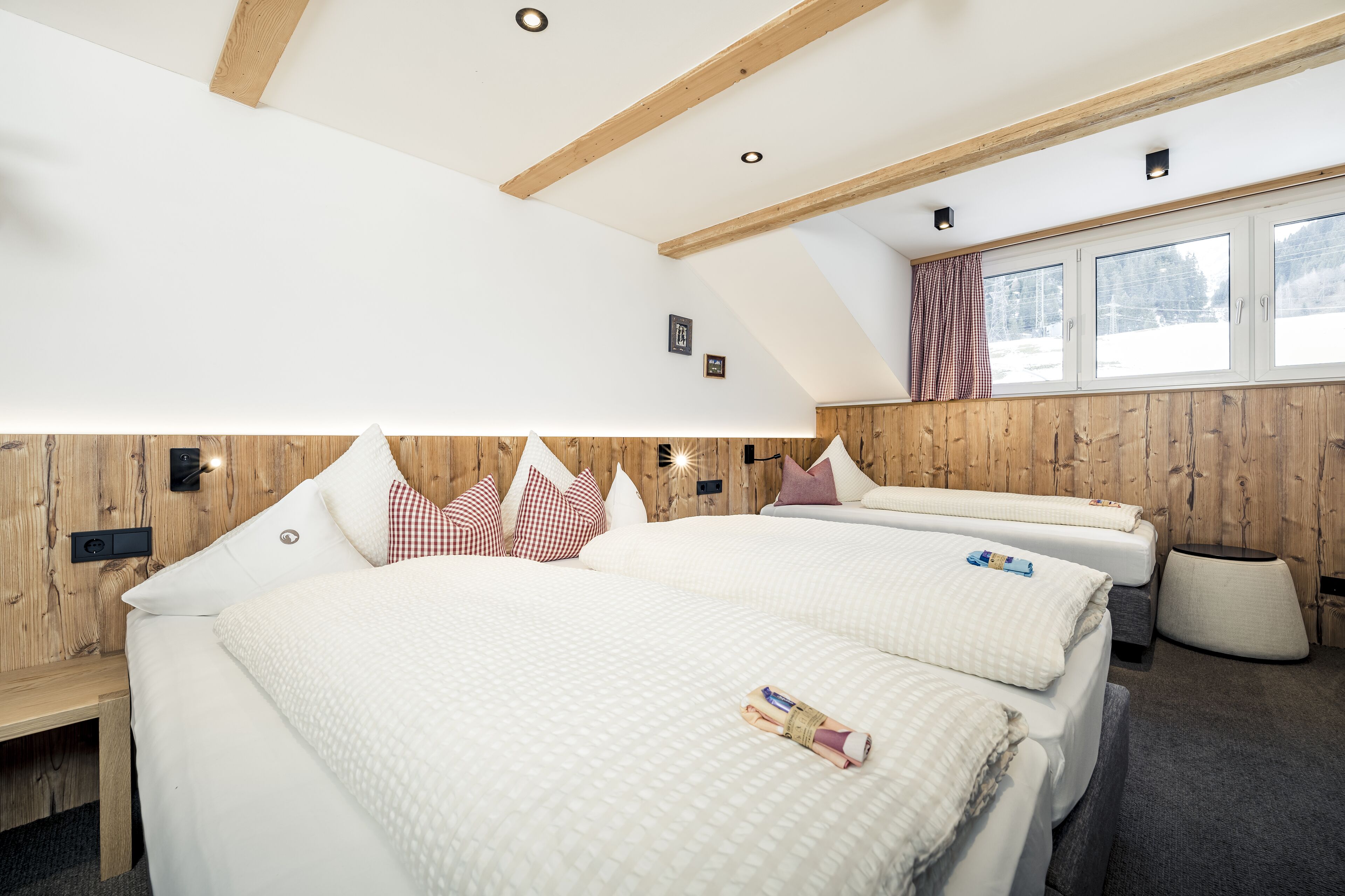 A modern hotel room with two beds, wooden paneling, a large window with a view, and a small bedside table.