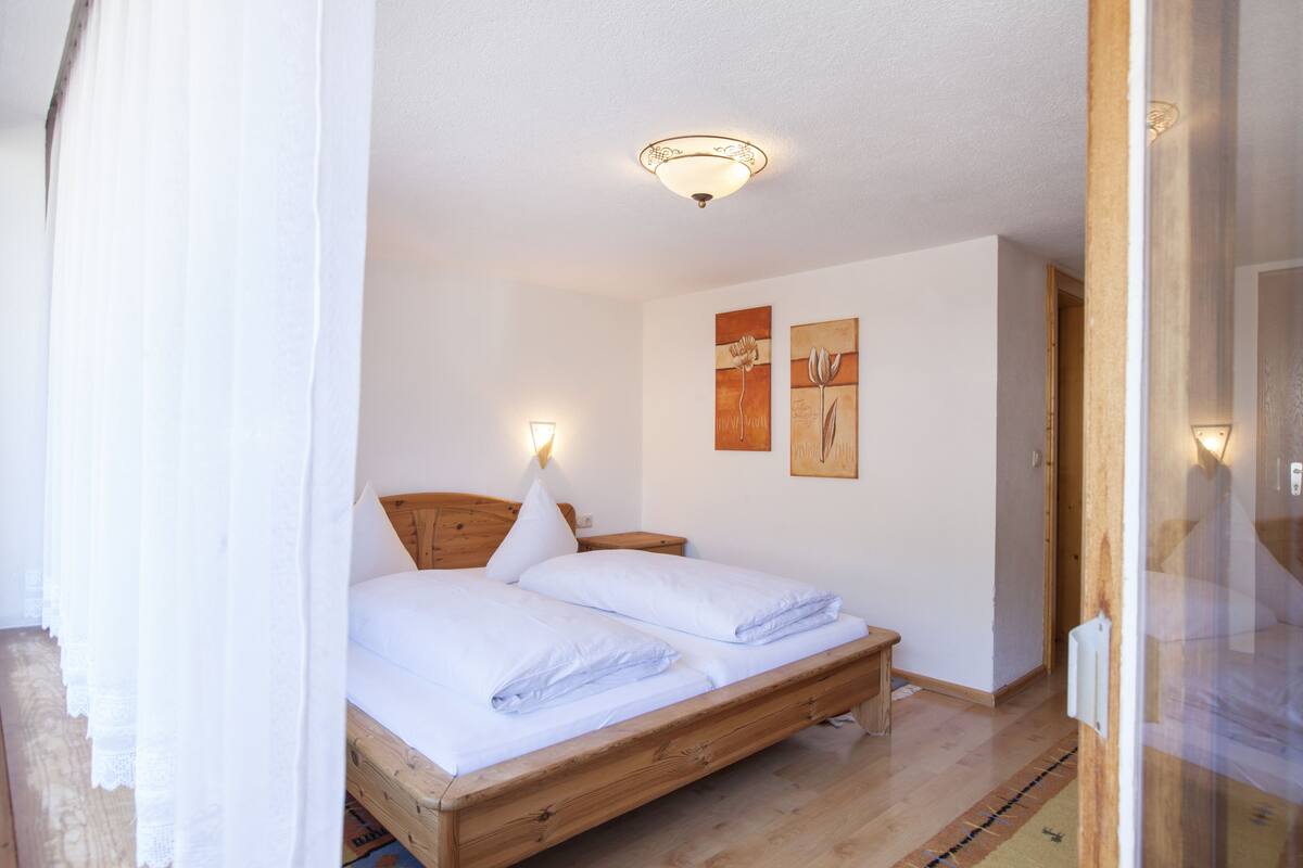 Un dormitorio con una cama de madera, ropa de cama blanca, una mesita de noche y decoración en la pared.