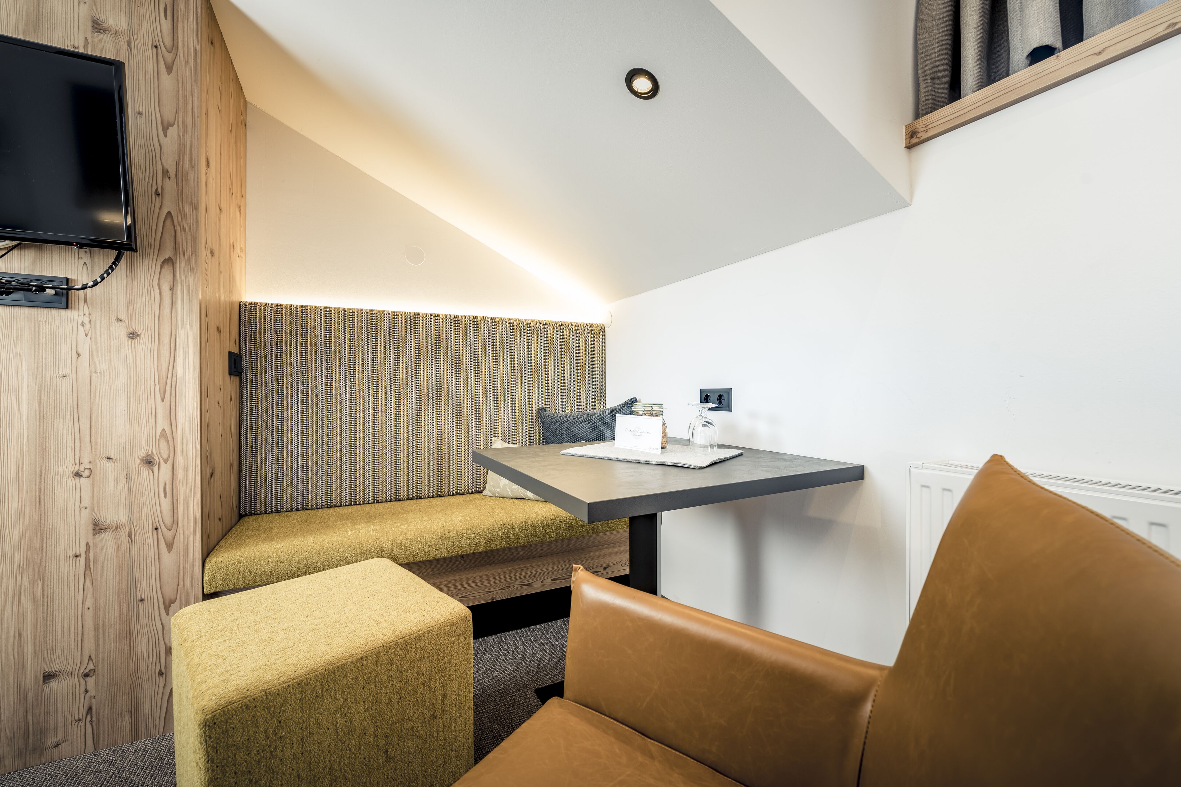 Una habitación moderna con pared de madera, televisor, banca, mesa y silla.