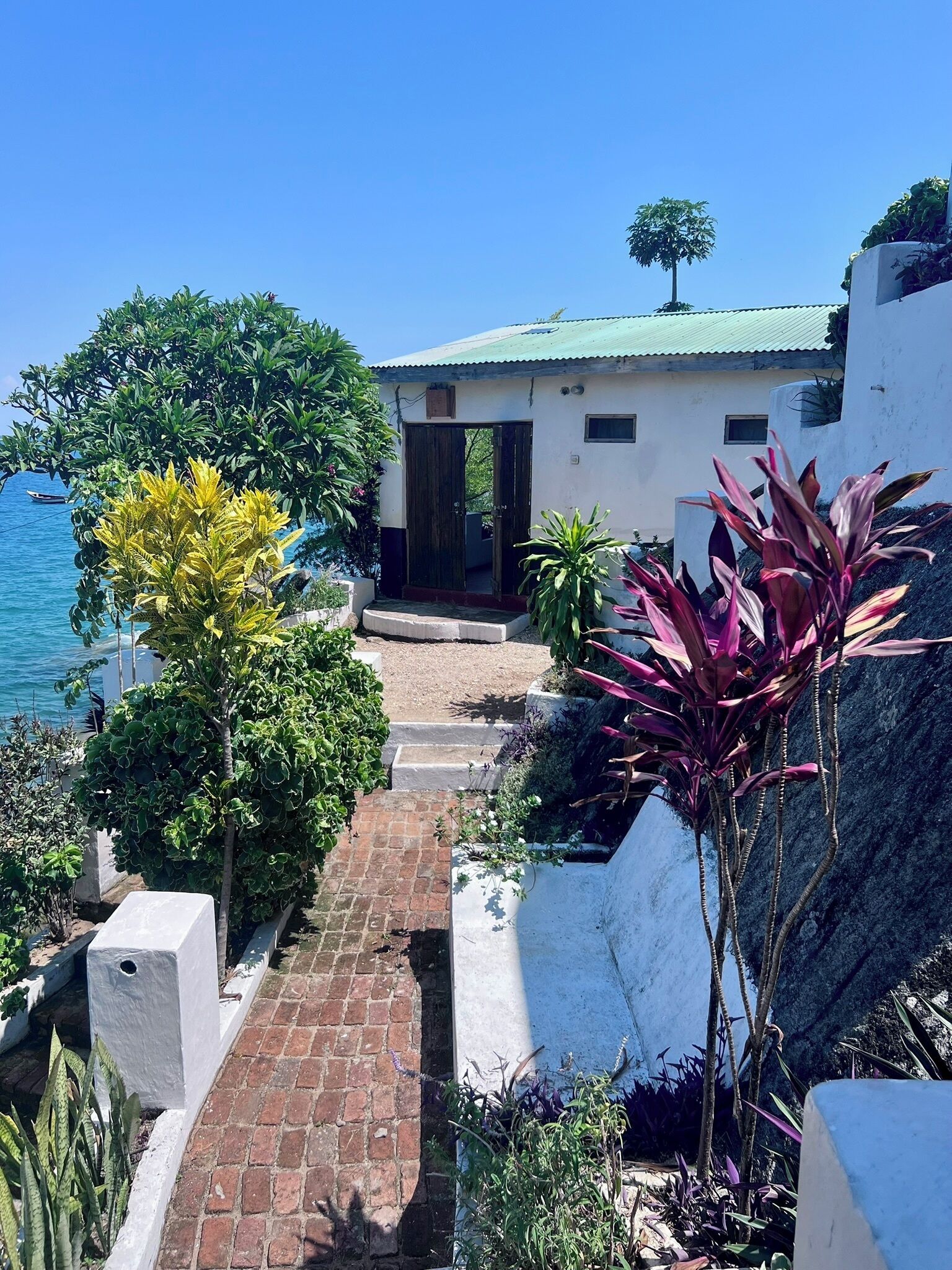 A coastal property with a paved pathway leading to a white building with a green roof.