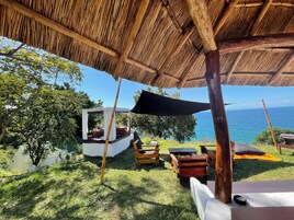 A thatched-roof outdoor seating area with a view of the sea.