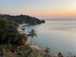 A coastal view with a beach, a gazebo, and a row of houses along the water.