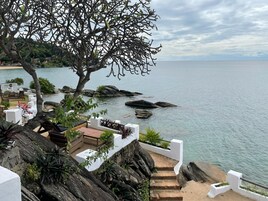 A coastal resort with a view of the sea, a tree-lined pathway, and outdoor seating areas.
