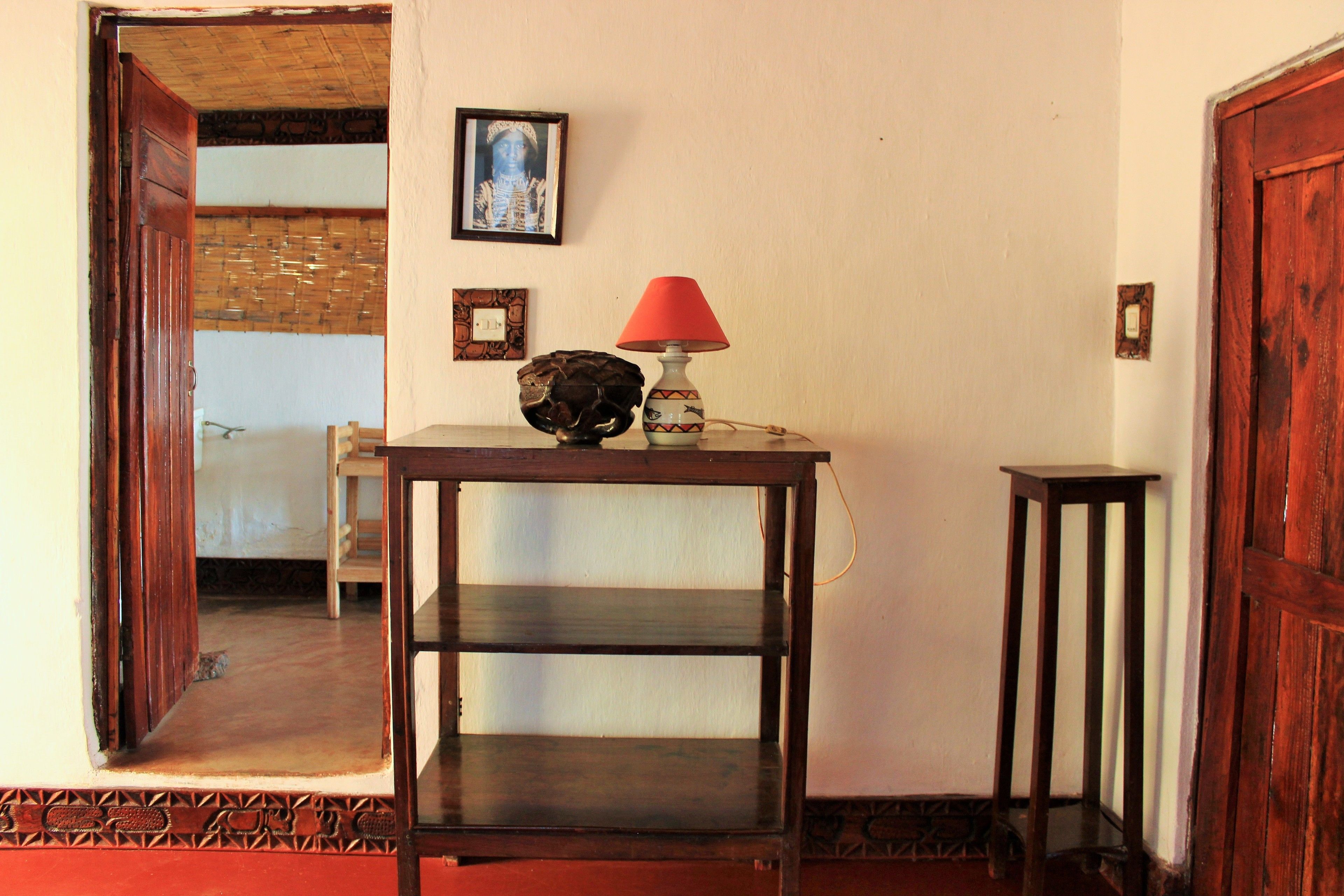 Una habitación con una mesa de madera, una lámpara roja y un cuadro de un esqueleto en la pared.