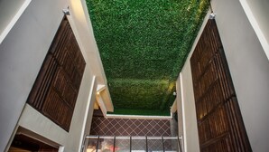 A corridor with a green artificial ceiling, wooden doors, and a view of a room with a control panel. - Armenian Suite (George Town)