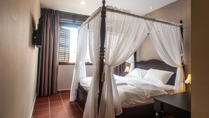 A four-poster canopy bed with white linens, a nightstand, and a bedside lamp. - Armenian Suite (George Town)