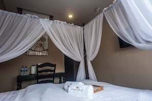 A hotel room with a four-poster bed, a nightstand with water bottles, a lamp, and a decorative wall piece.