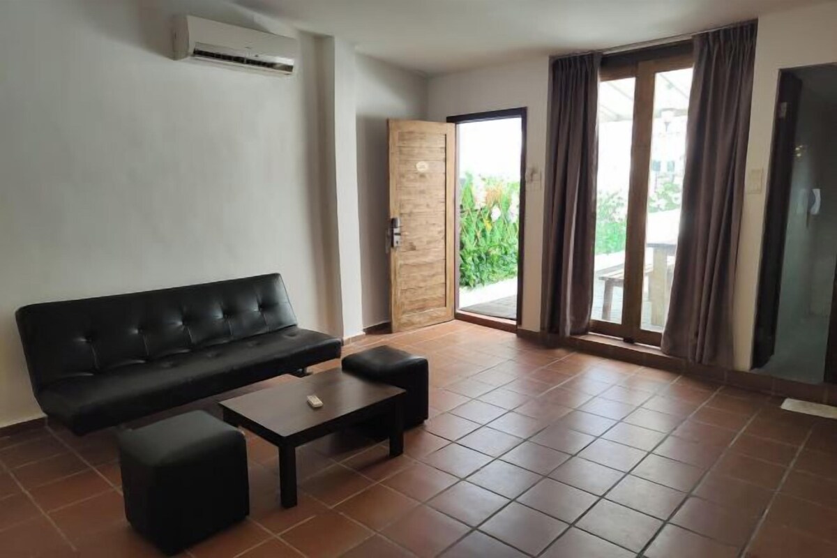 Una sala de estar con un sofá negro, una mesa de centro y un ventanal corredero que da a un área exterior.
