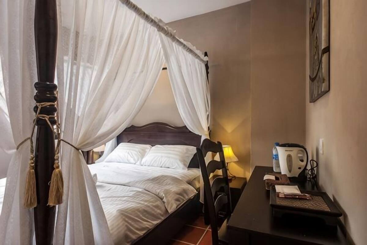 A room with a bed, a chair, a table, and a wall-mounted kettle.