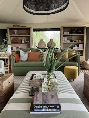 Een gezellige woonkamer met een groene bank, een bijzettafeltje met boeken en een vaas, en een groot raam met natuurlijk licht.