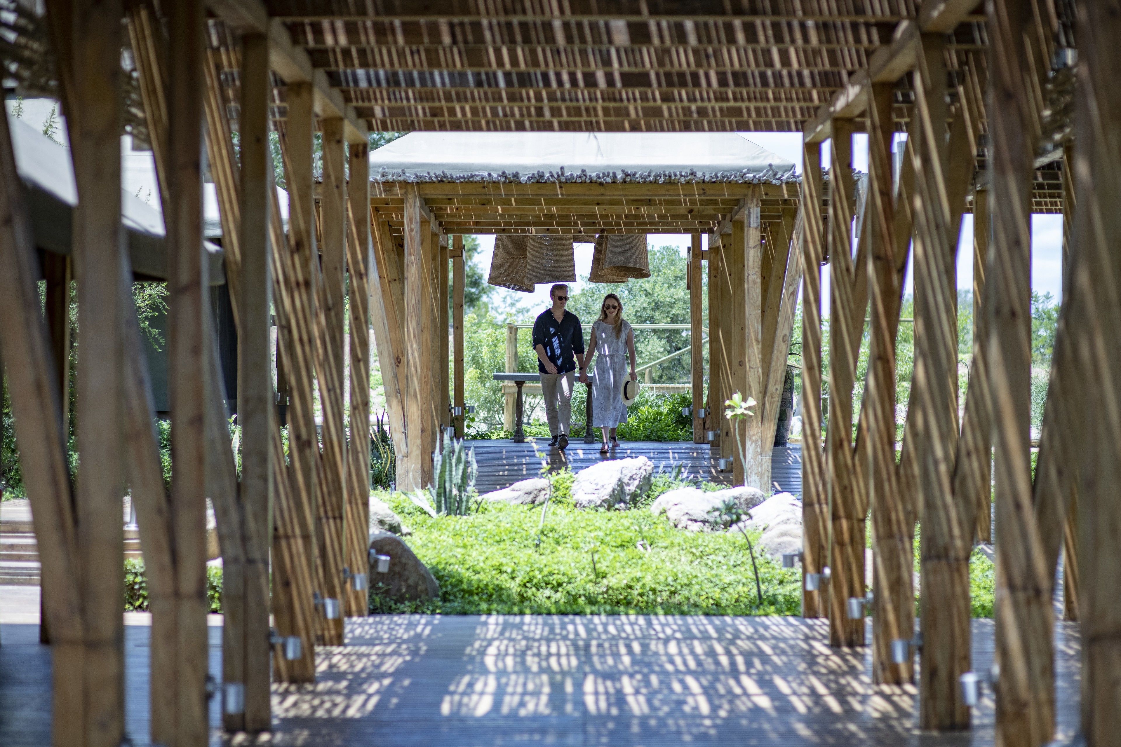 A wooden pavilion with a thatched roof, surrounded by greenery and rocks.