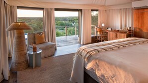 Un'ampia camera da letto con un letto grande, un angolo salotto con vista e un balcone con tavolo e sedie.