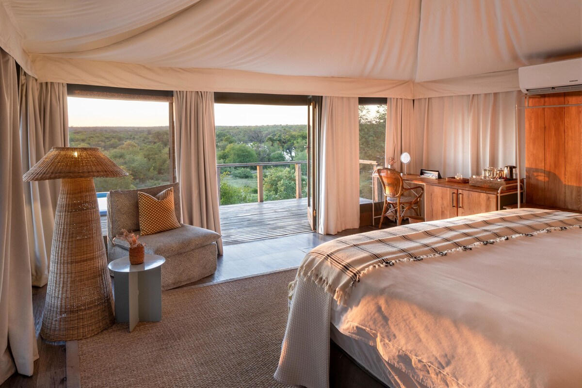 Een ruime slaapkamer met een groot bed, een zithoek, een bureau en een balkon met uitzicht.