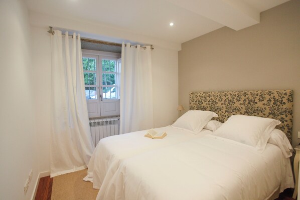 Un dormitorio con cama, cortinas blancas, ventana y radiador.
