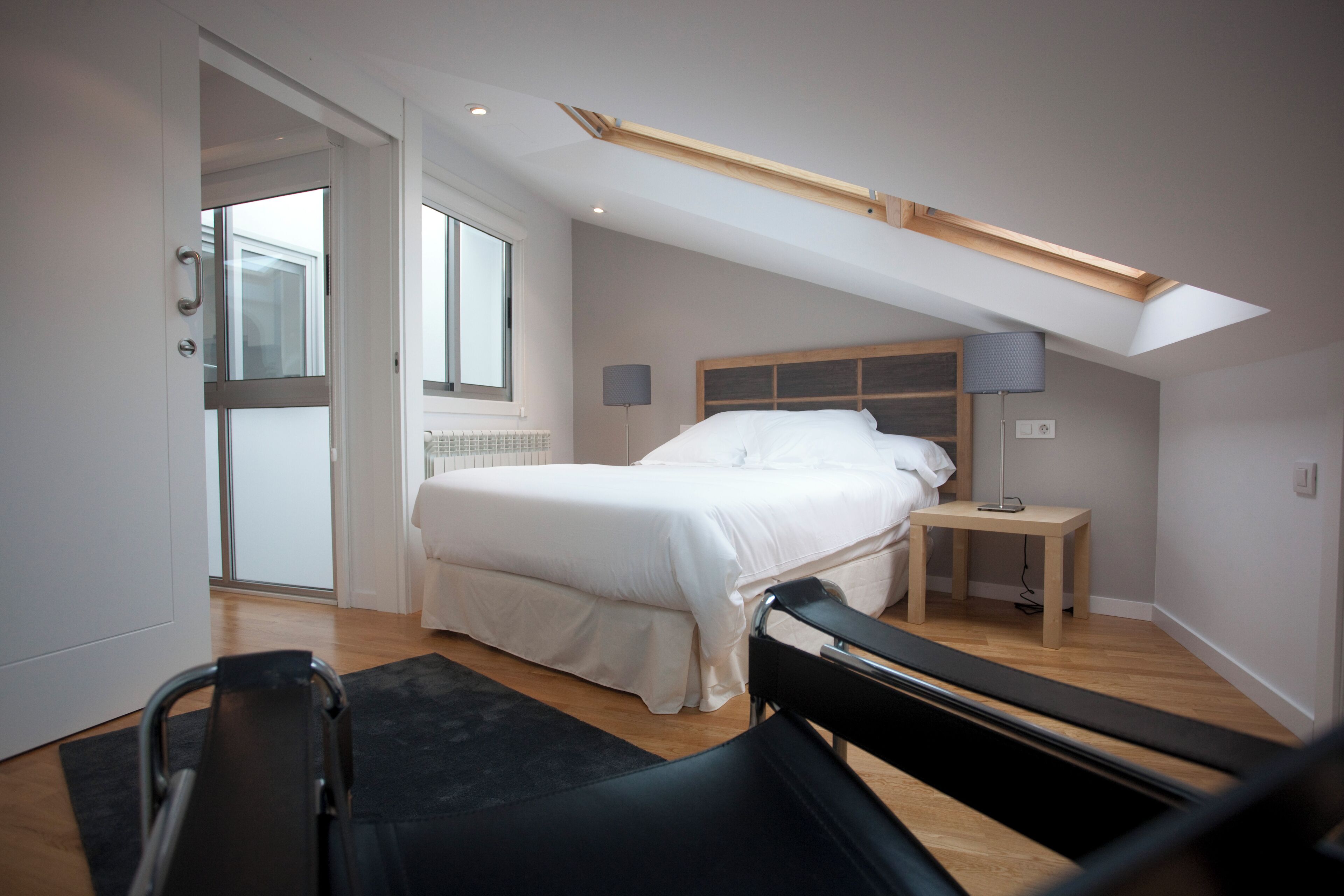 Un dormitorio con cama, mesita de noche, lámpara y tragaluz.