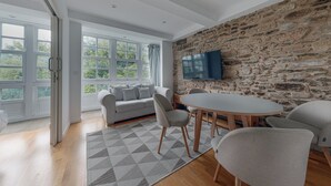 Una sala de estar moderna con una pared de piedra, un ventanal grande, un sofá, un televisor y un comedor.
