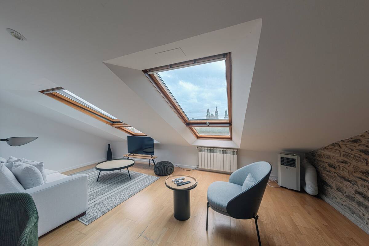 A modern loft apartment with skylights, a sofa, a chair, a small table, and a radiator.