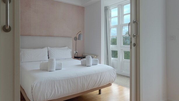 Un dormitorio con una cama grande, una mesita de noche, una lámpara y una ventana con vistas a la vegetación.