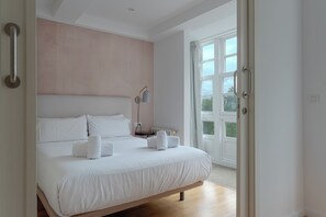 A bedroom with a large bed, a bedside table, a lamp, and a window with a view of greenery. - Catedral Site by Como en Casa (Santiago de Compostela)