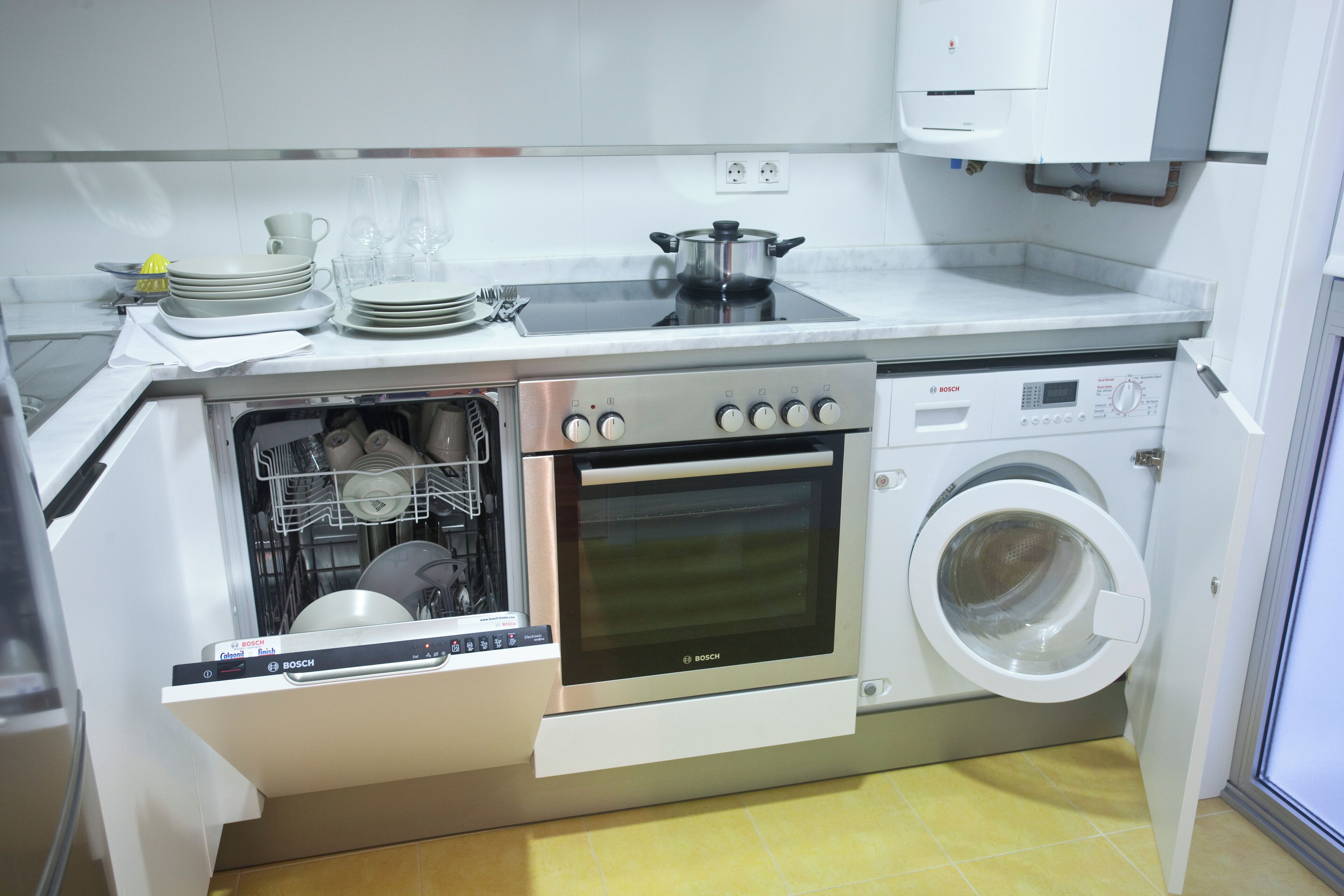 A compact kitchen with a Bosch dishwasher, oven, and washing machine integrated into the cabinetry.