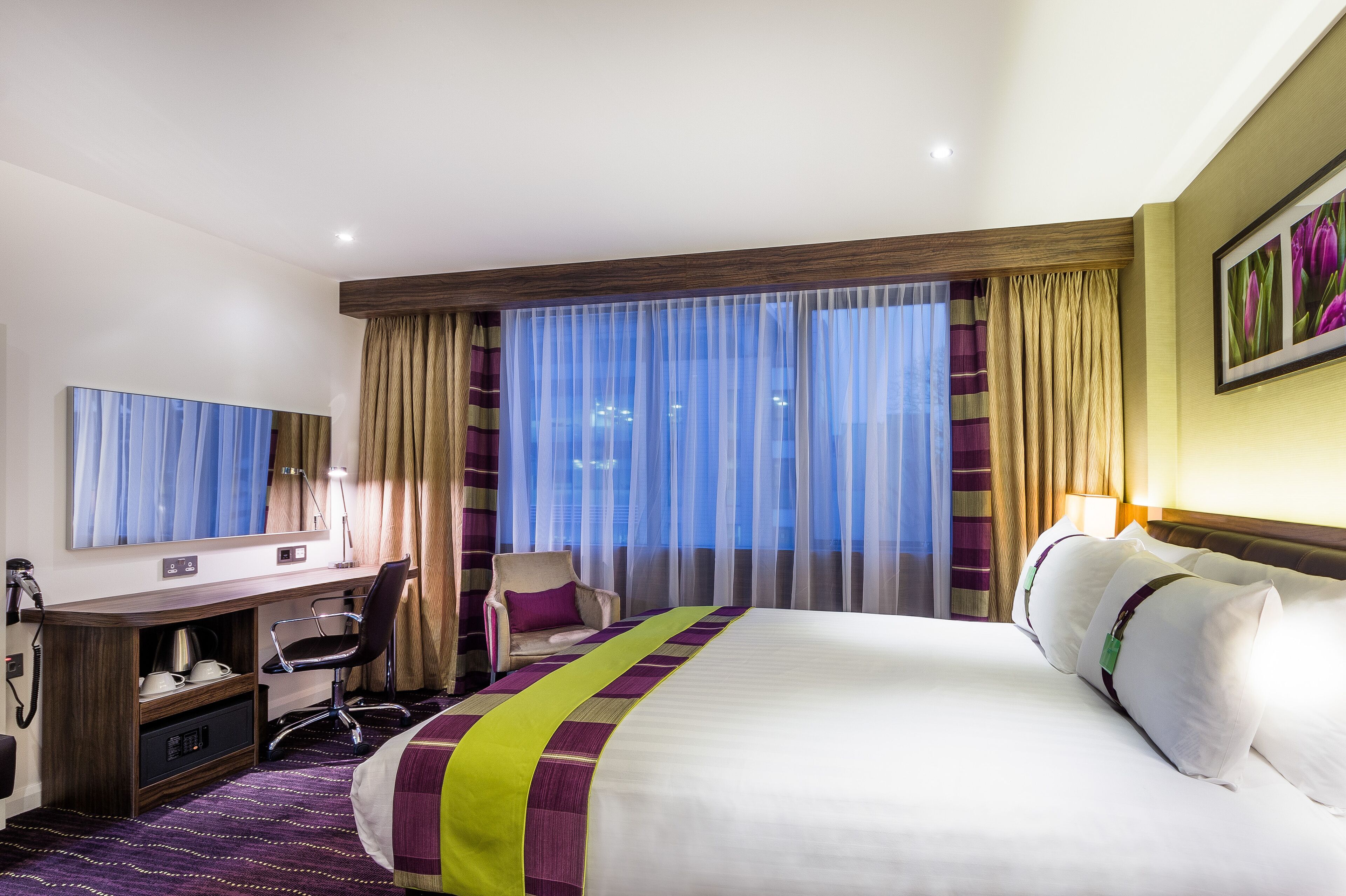 Una habitación de hotel con una cama grande, un escritorio con silla, un televisor y una ventana con cortinas.