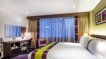 Una habitación de hotel con una cama grande, un escritorio con silla, un televisor y una ventana con cortinas.