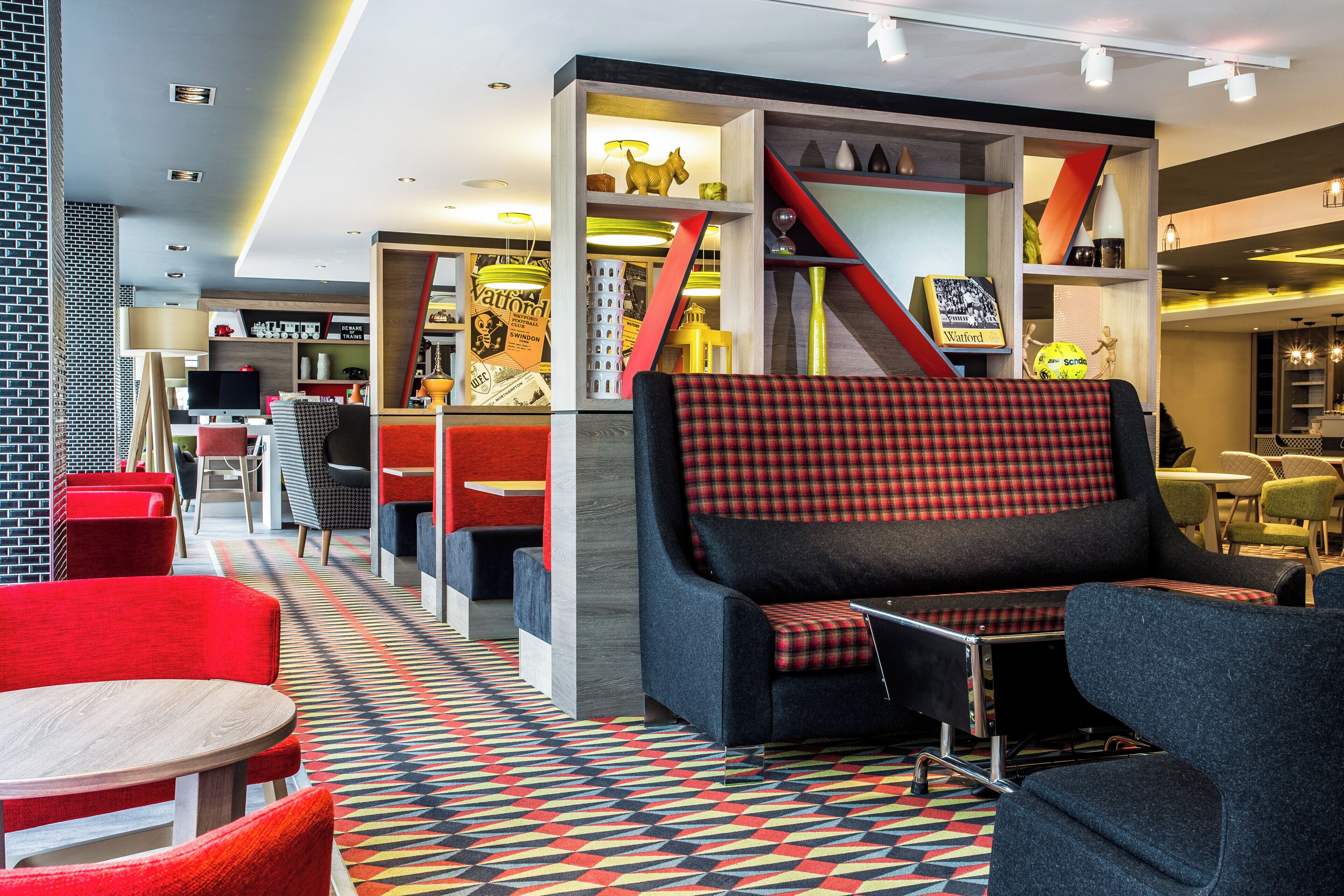 Un área de estar moderna con piso de diseño geométrico, asientos tapizados en rojo y negro, y una variedad de objetos decorativos en estanterías.