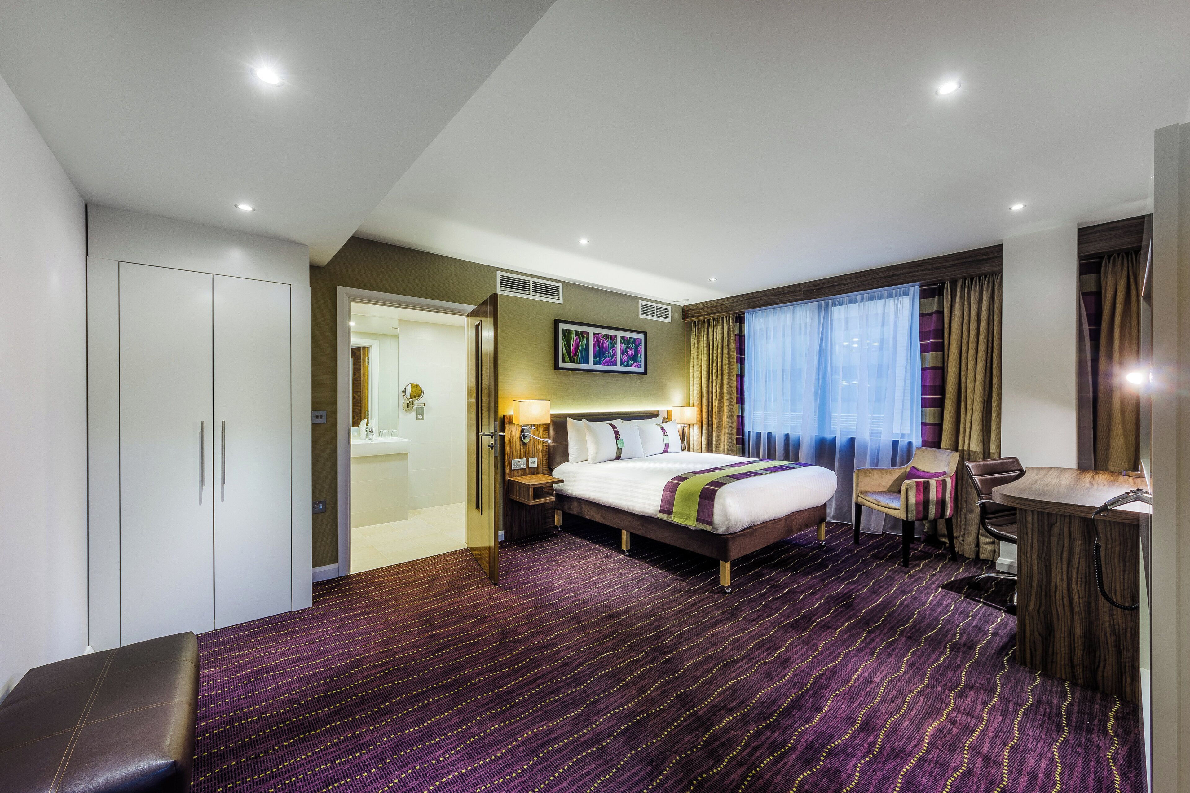 A hotel room with a bed, a desk, a chair, a wardrobe, and a television.
