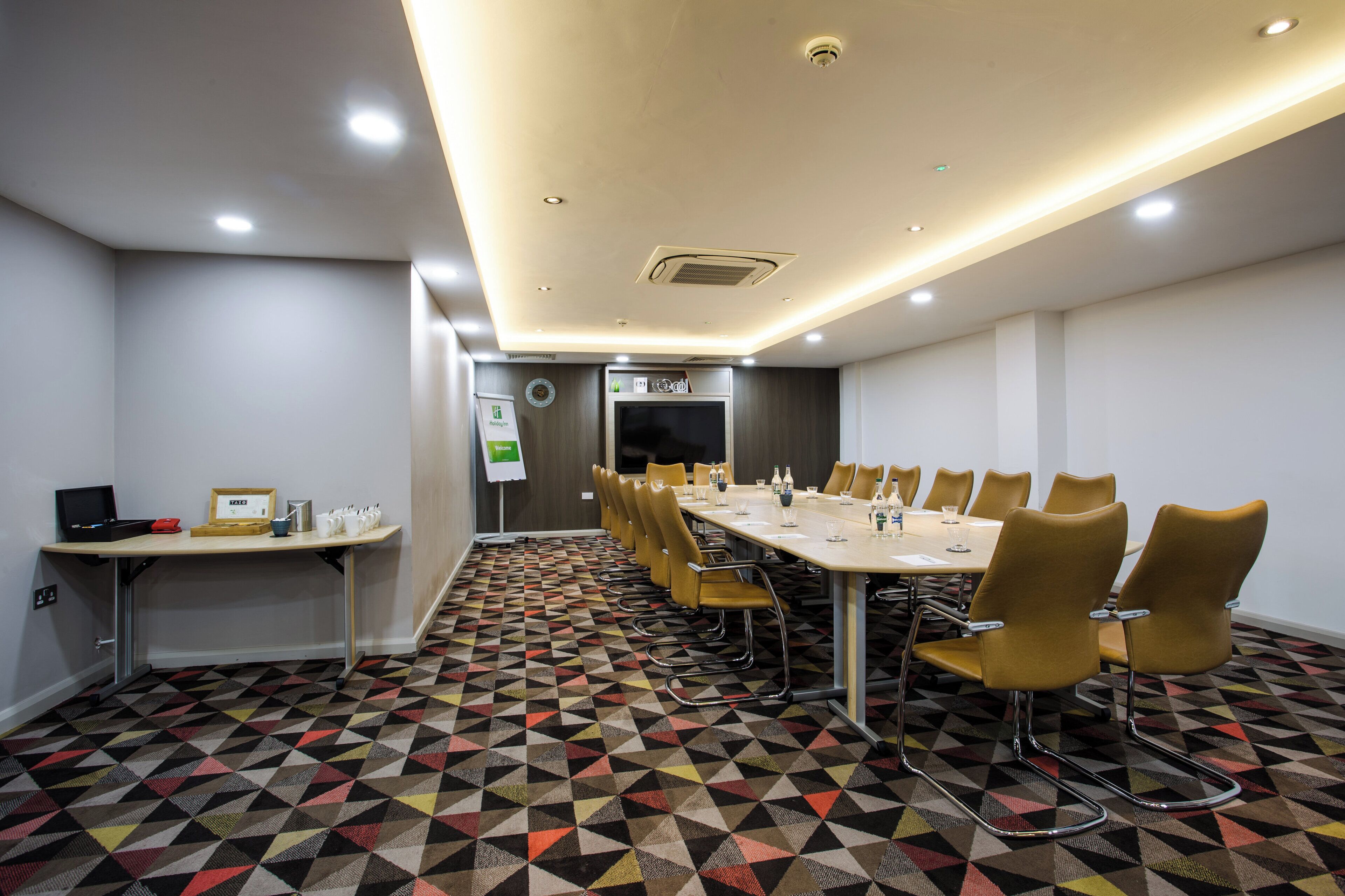 Un salón de conferencias con una mesa larga, sillas y una alfombra estampada.